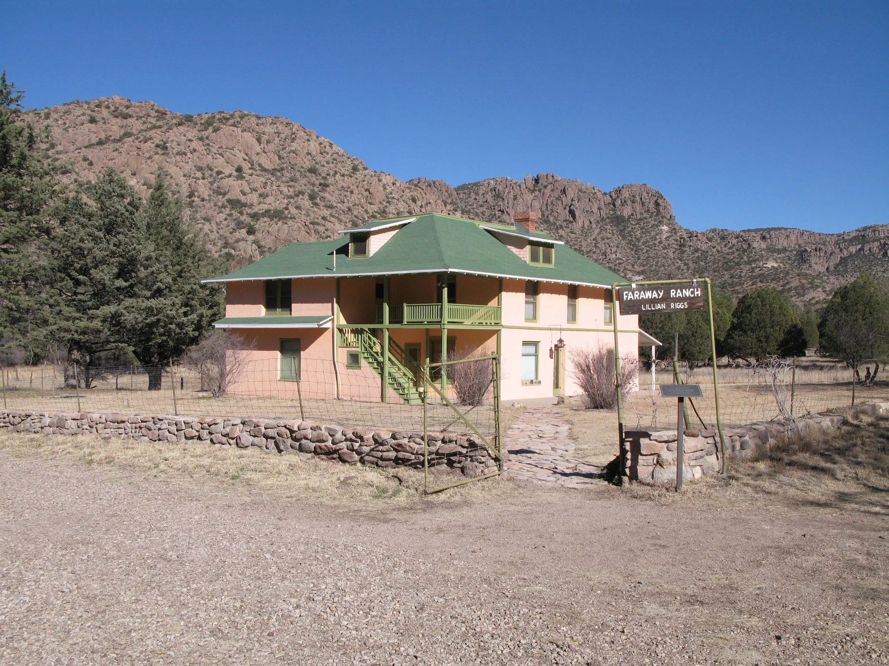 Peach-colored Faraway Ranch house with a green roof, exterior stairs and a rocky ridge behind it.