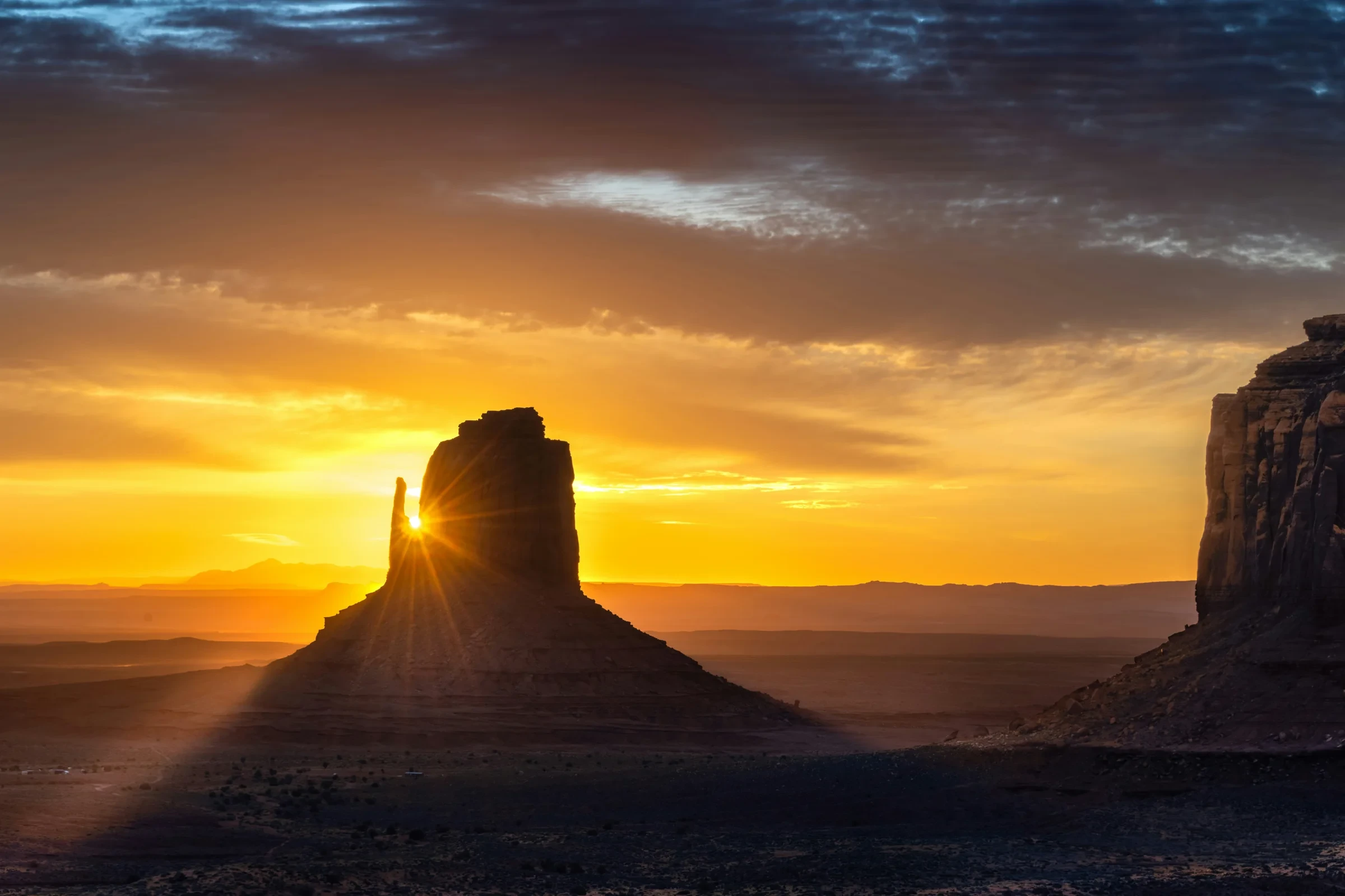 A sandstone butte silhouetted against golden light in Monument Valley.