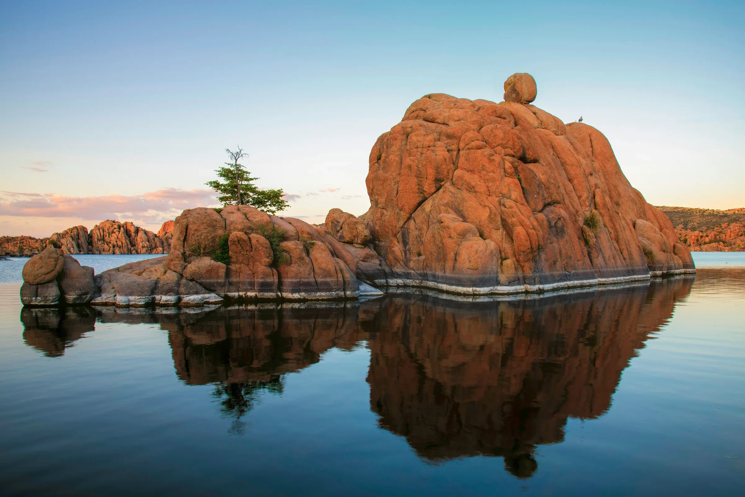 Rounded orange granite boulders and their reflections in Watson Lake.