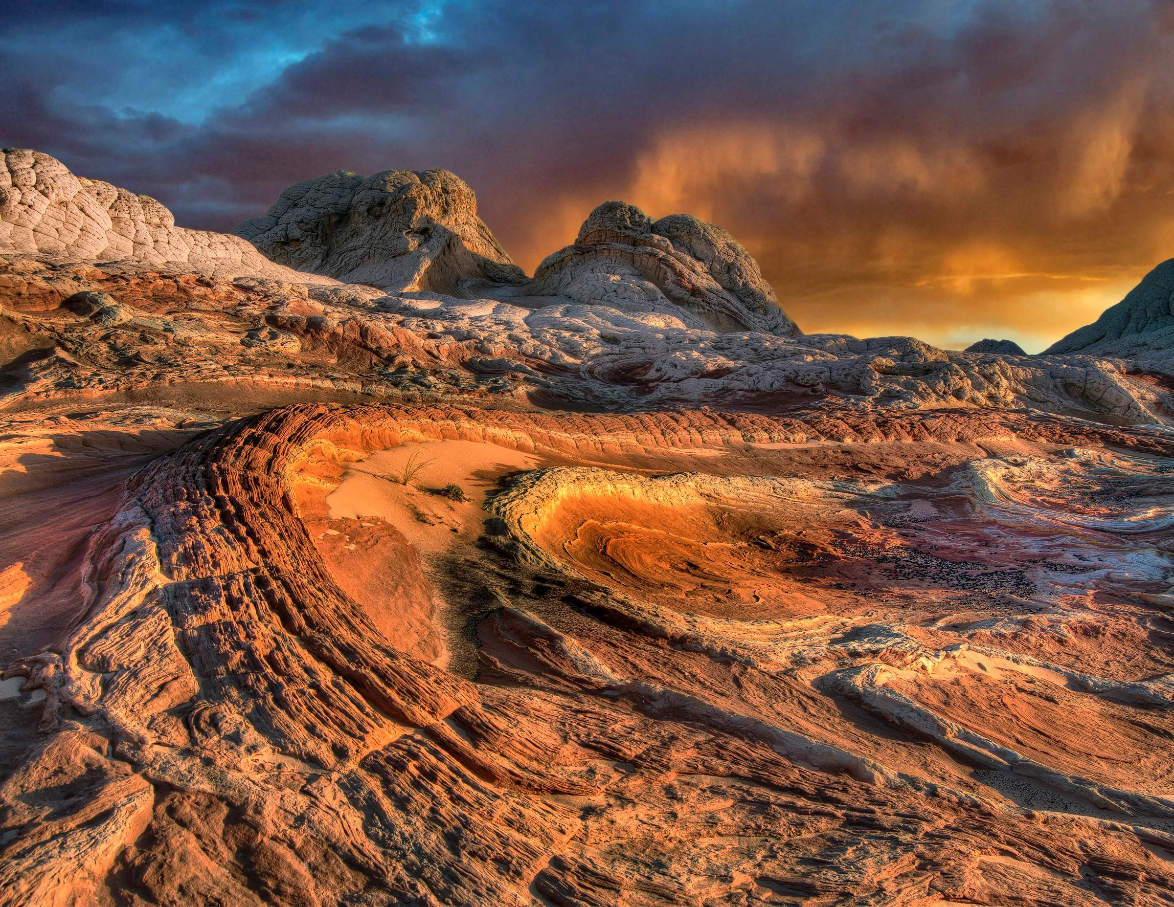 Pale domes and rippled orange sandstone at White Pocket beneath dramatic clouds.