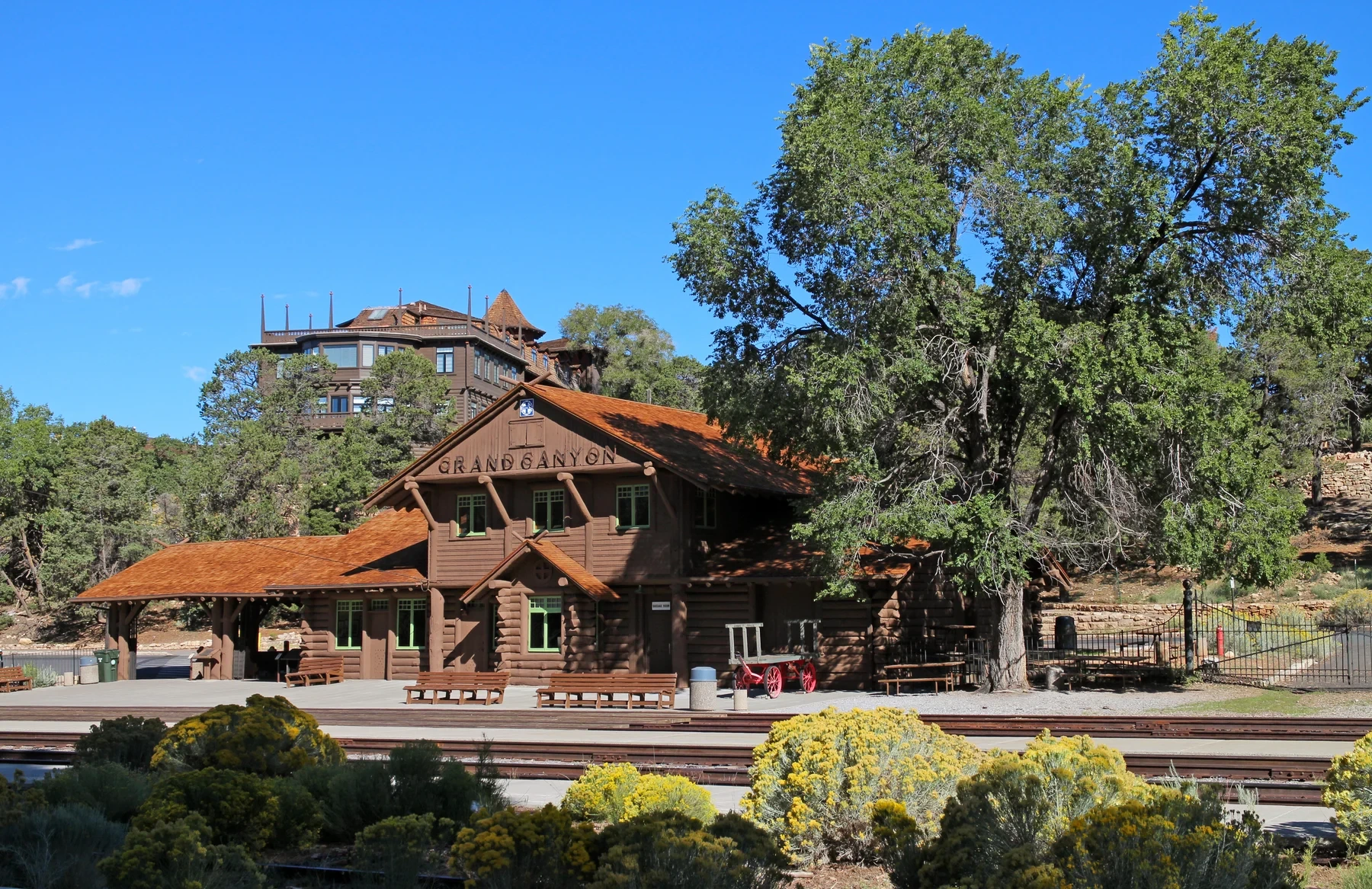 The log Grand Canyon depot beneath trees with El Tovar rising behind it.