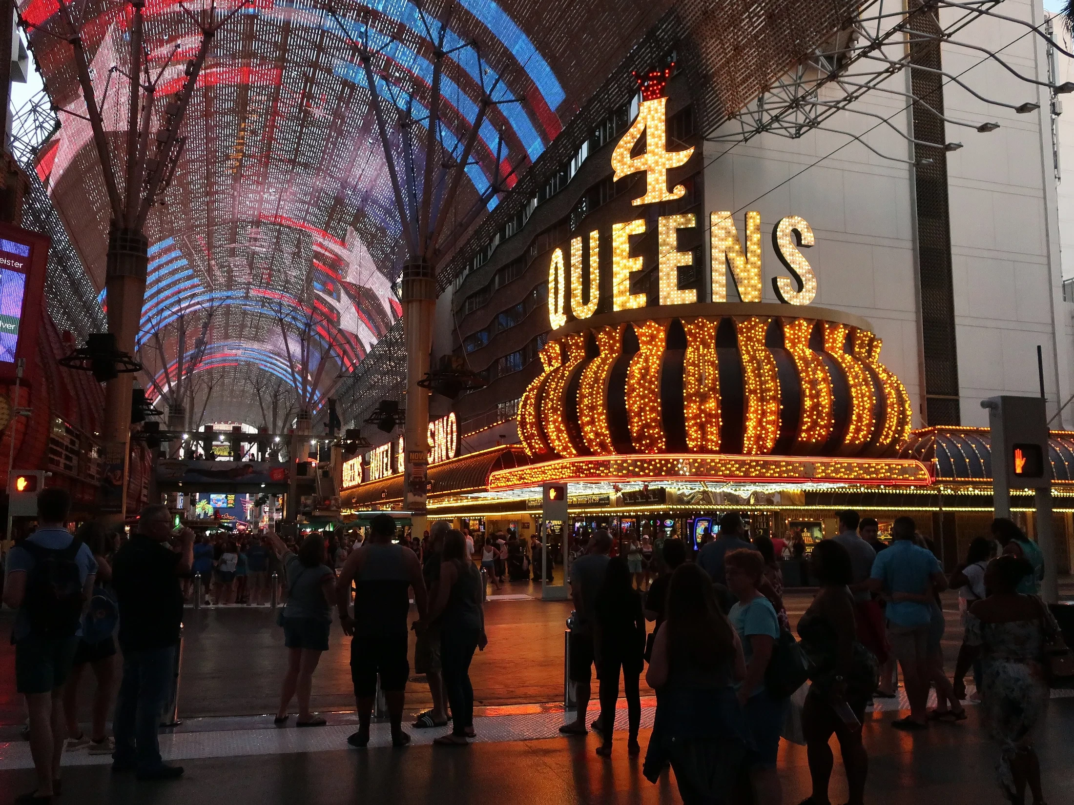 The illuminated Four Queens sign and pedestrians beneath the Fremont Street Experience canopy at night.