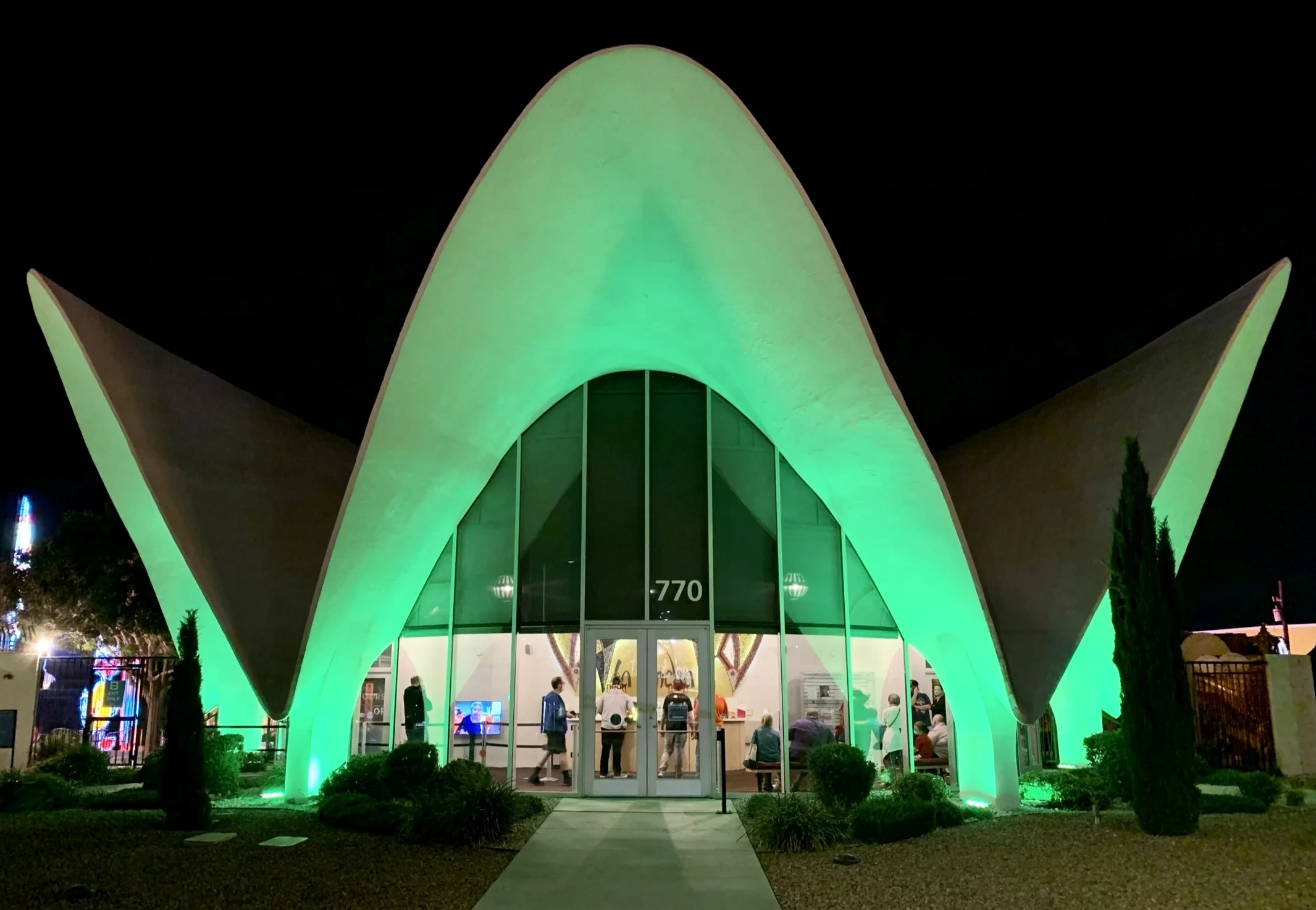 The curved white shell roof of the former La Concha Motel lobby, illuminated green at the Neon Museum entrance.