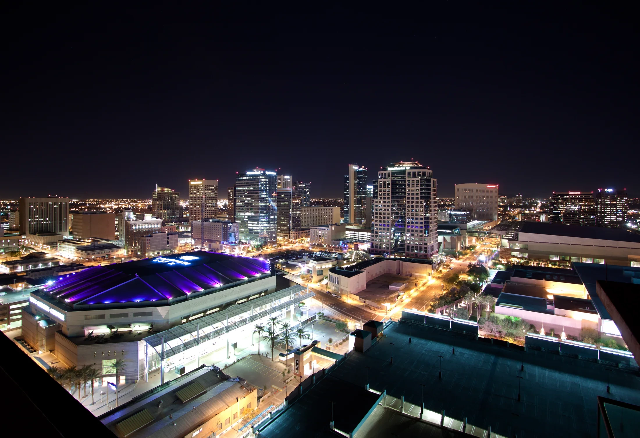 Downtown Phoenix buildings and streets illuminated at night beneath a dark sky.