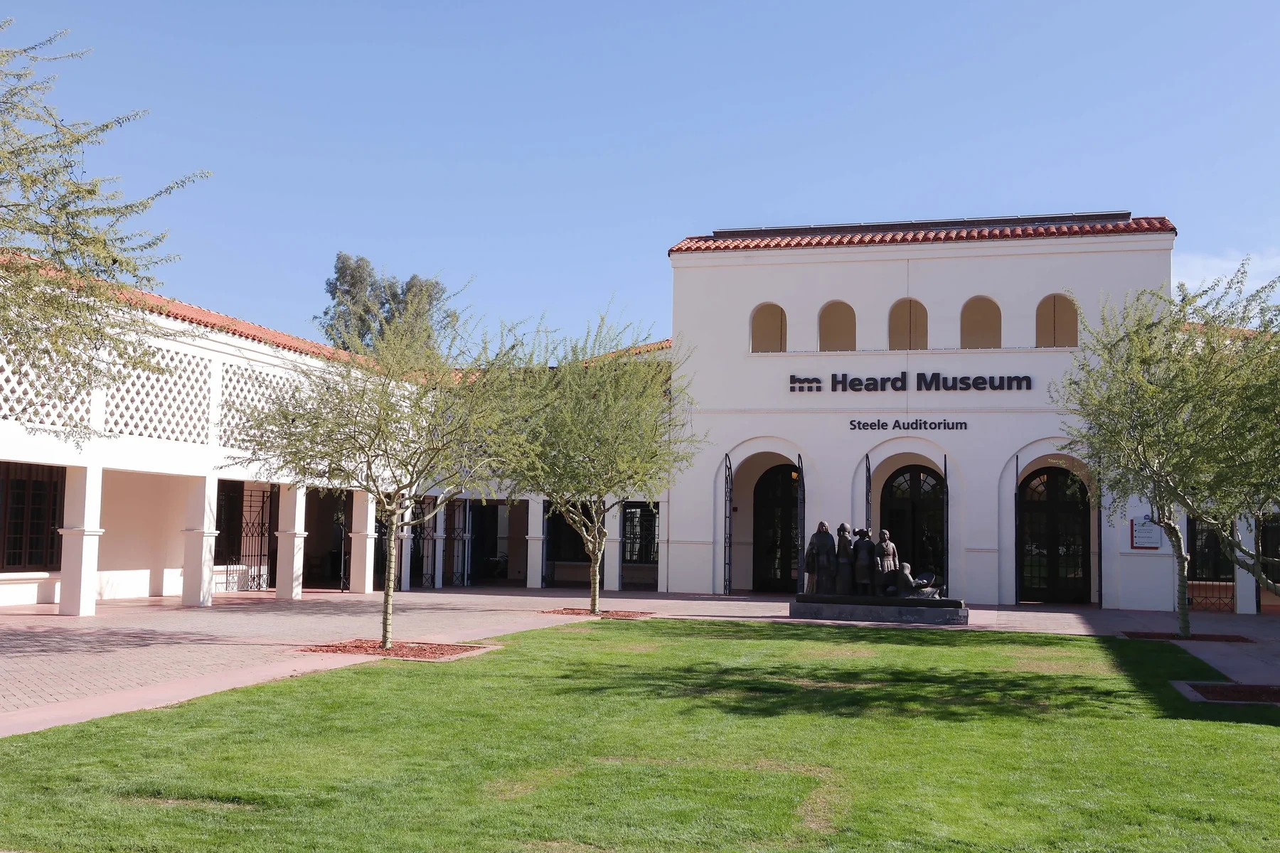 White stucco arcades and the Heard Museum auditorium face a courtyard with trees and lawn.