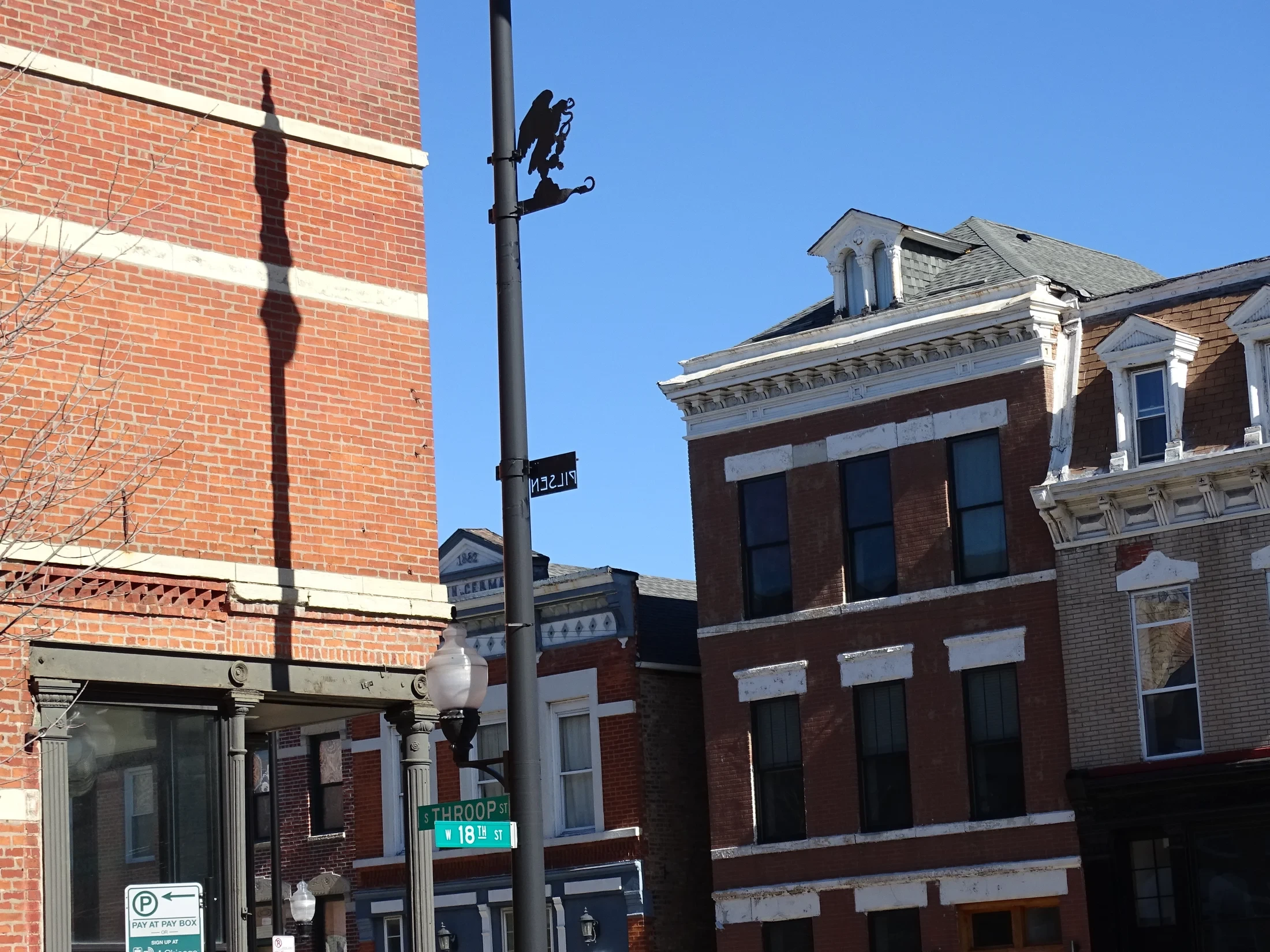 Brick buildings and decorative cornices beside the 18th Street and Throop Street signs in Pilsen.