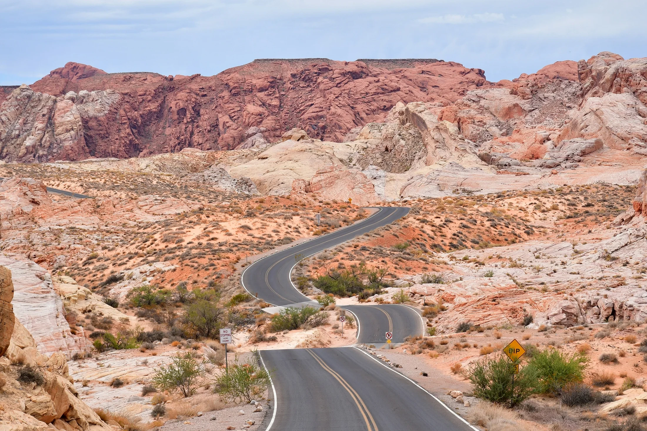 A winding paved road between pink, cream and red sandstone formations in Valley of Fire State Park.
