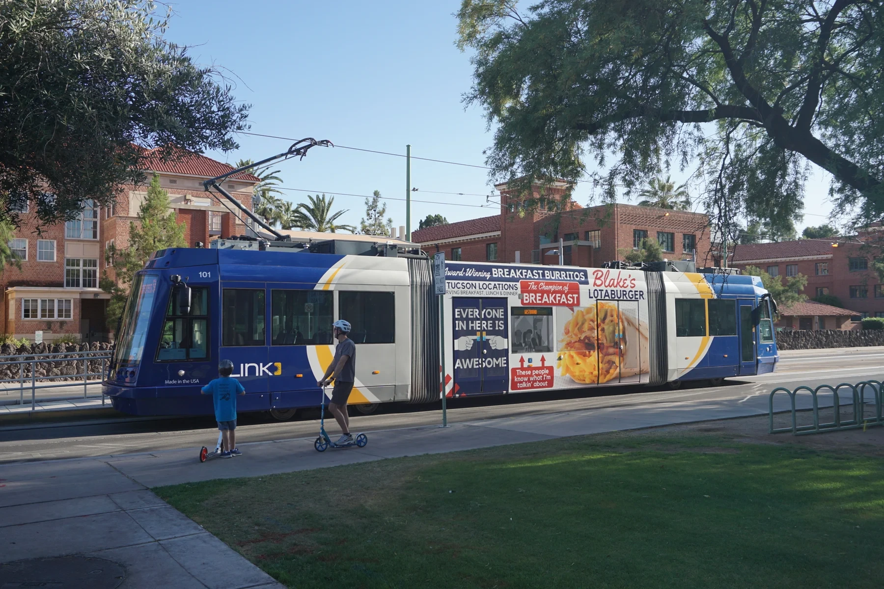A blue Sun Link streetcar beside red-brick university buildings in Tucson.