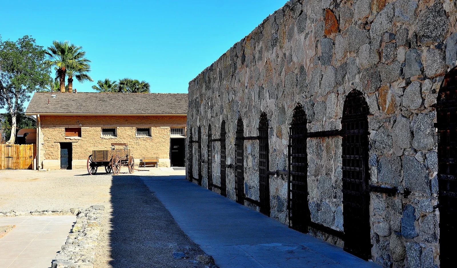 Stone cellblock with barred arched entrances beside a courtyard at Yuma Territorial Prison.