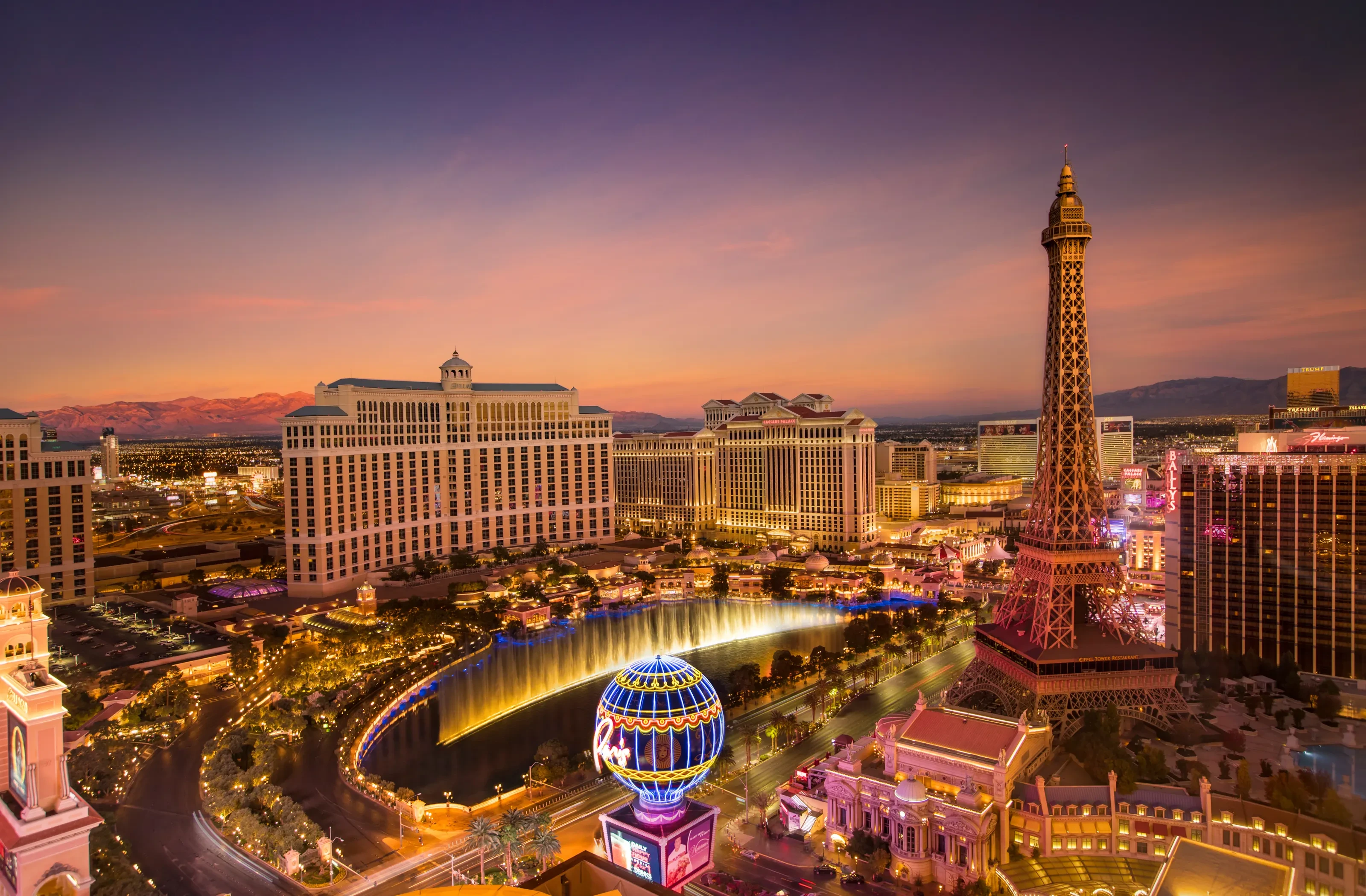 The Bellagio fountains and Paris Las Vegas illuminated beneath a rose-colored evening sky