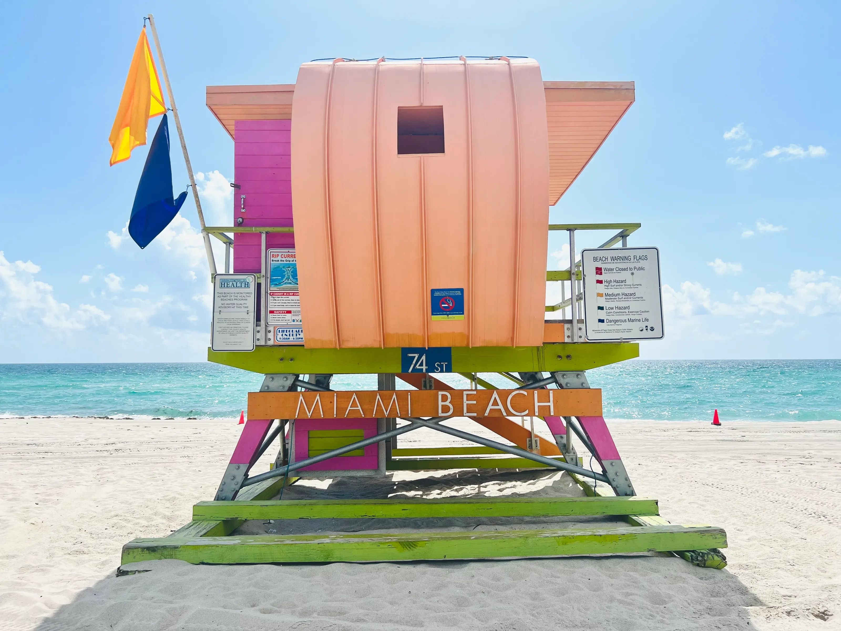 A pink, orange, and lime-green Miami Beach lifeguard tower beside turquoise water
